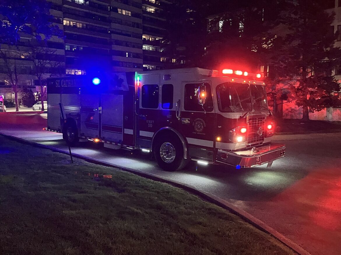 Nighttime fire engine with red and blue emergency lights parked on a street in front of apartment buildings.