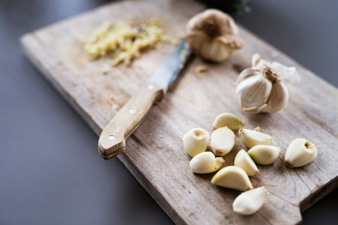 Garlic cloves scattered on a wooden cutting board with a knife nearby.