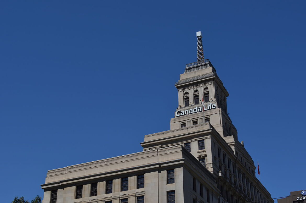 Beige stone office building with a tall tower and a Canada Life sign atop, set against a clear blue sky.