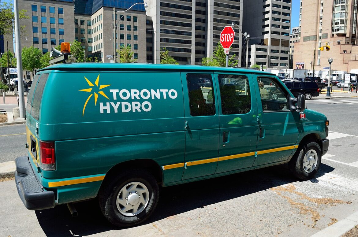 Teal Toronto Hydro service van parked on a city street with tall buildings in the background.