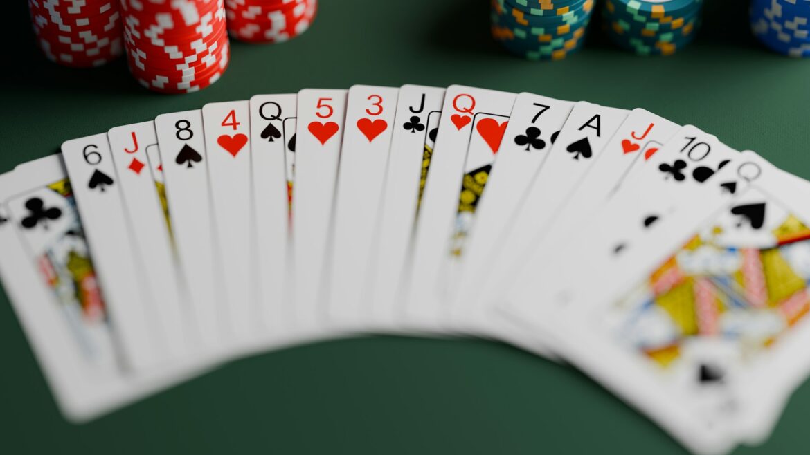 Fanned set of playing cards on a green poker table with stacks of colorful poker chips in the background.