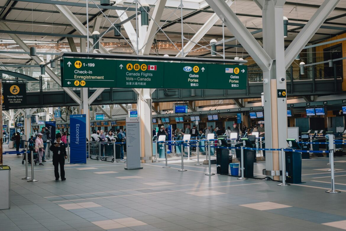 Signage in a spacious airport terminal directing to check-in, Canada flights, and gates D/E with passengers and counters nearby.