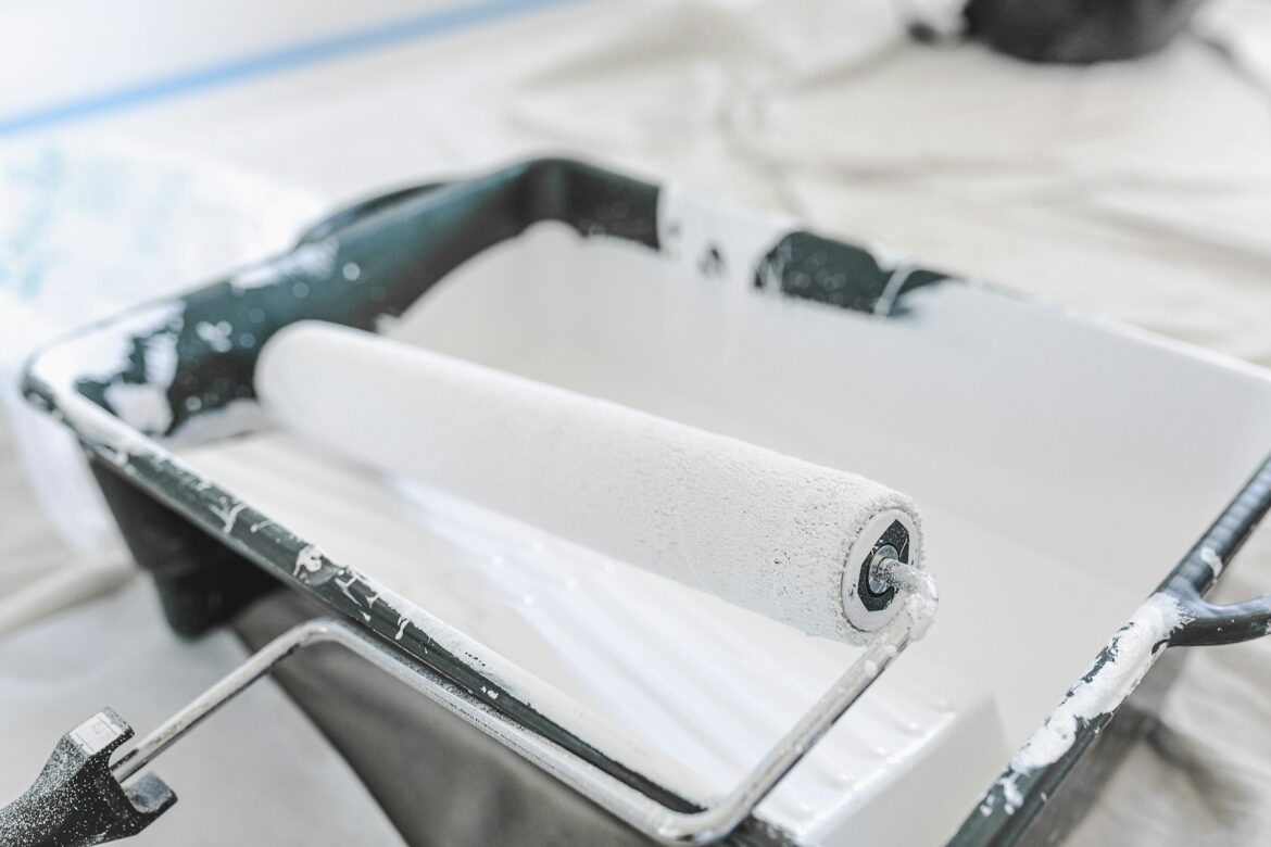 Paint roller with white paint residue resting on a metal frame in a painting setup.