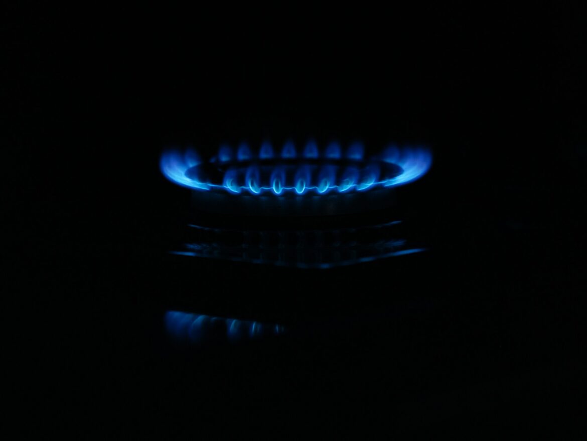 Blue gas flame on a stove burner glowing in darkness, with a ring of blue flames around the burner.