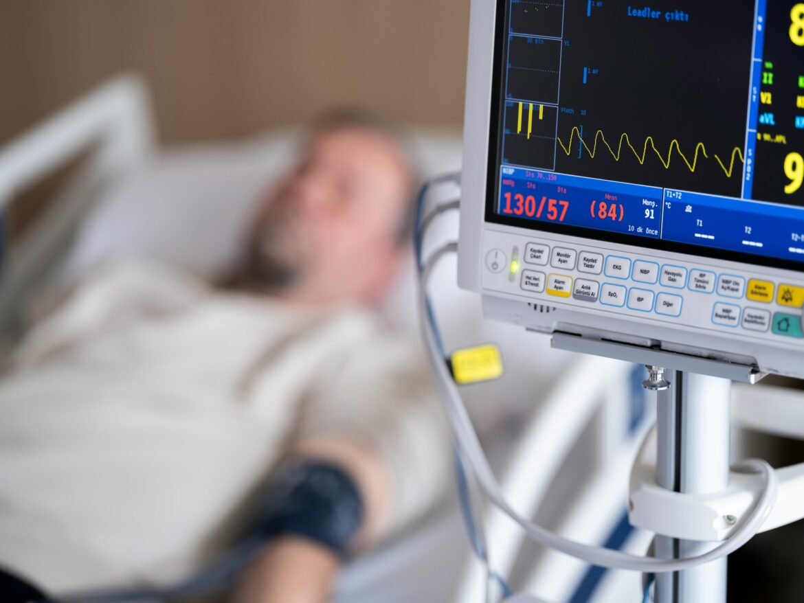 Hospital patient lying in bed connected to a monitor displaying vitals such as heart rate and blood pressure