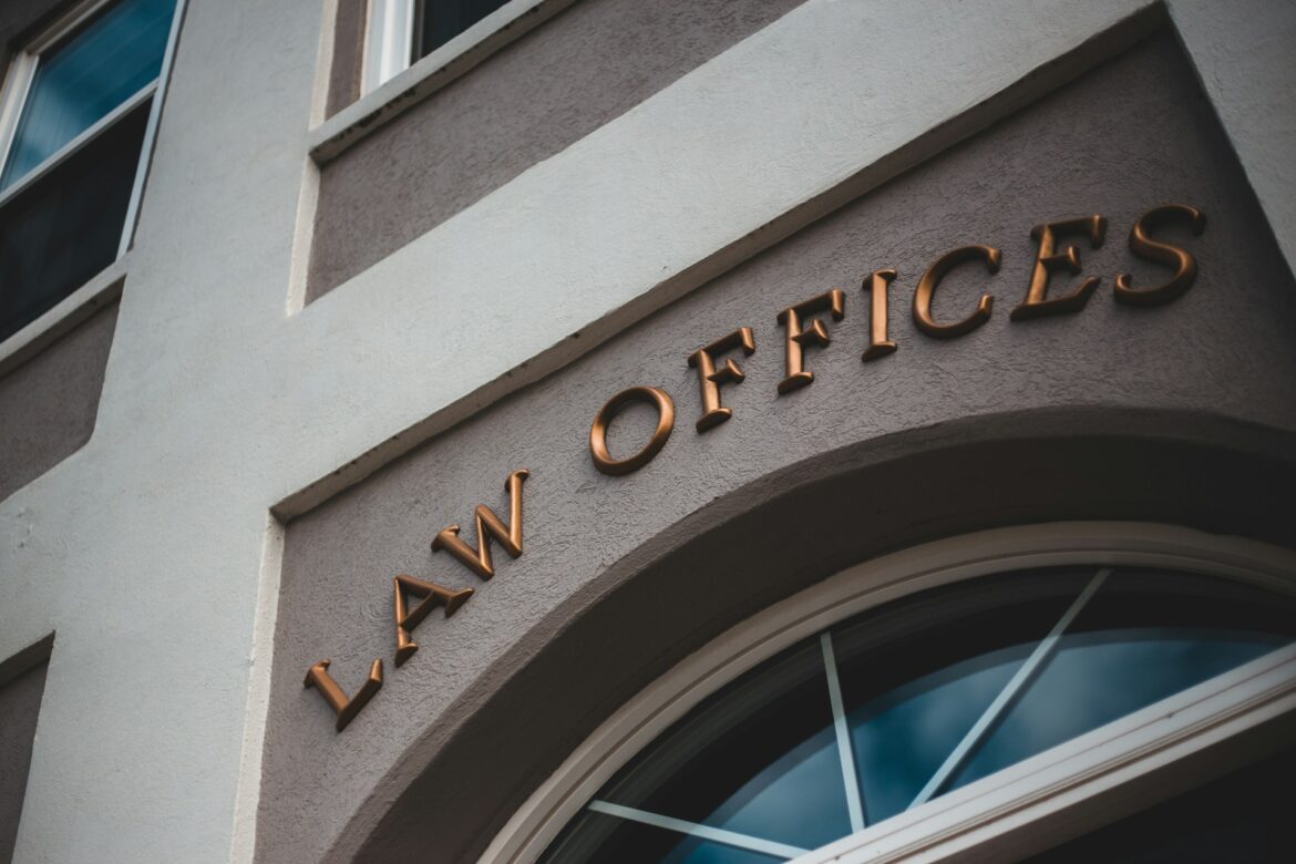 Copper letters spelling 'LAW OFFICES' mounted on a beige building facade above an arched window.