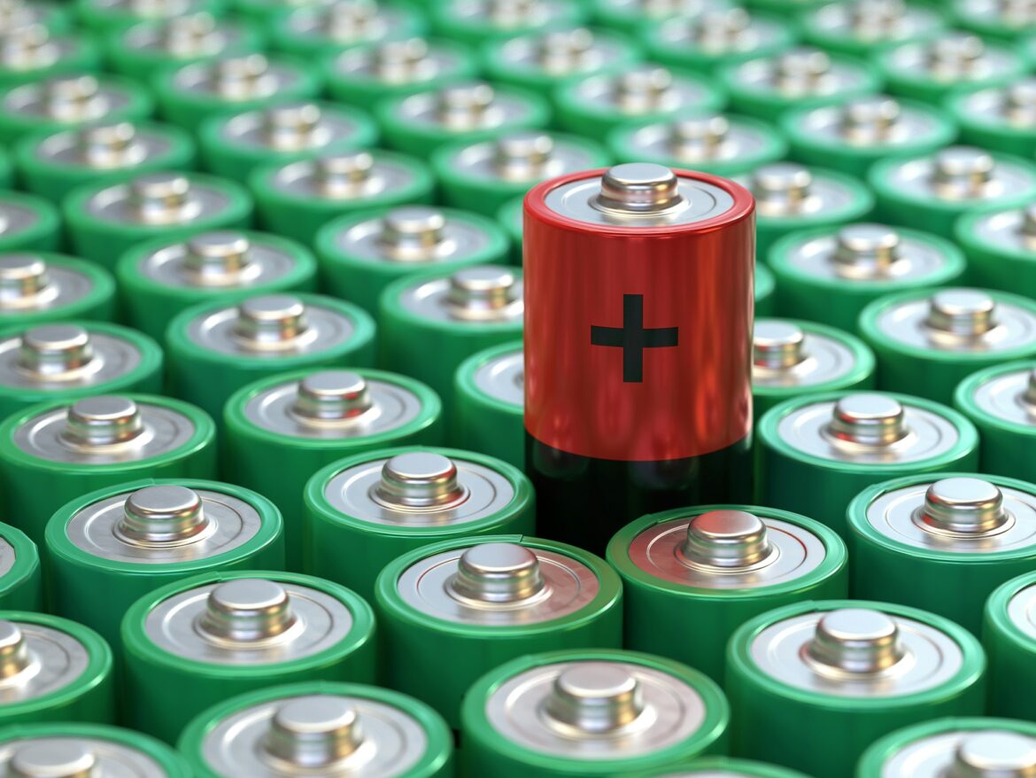 Close-up of a red battery with a plus sign standing out among many green batteries.