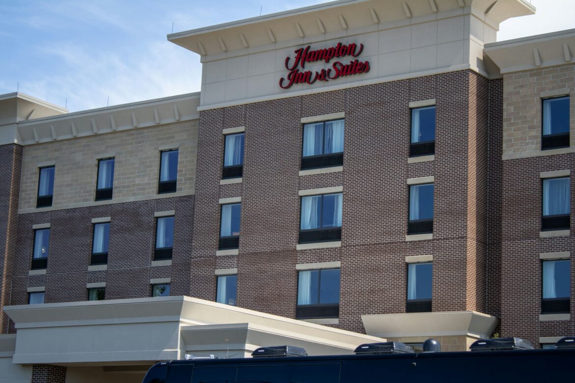 Hampton Inn & Suites exterior view showing brick facade and row of windows under a blue sky