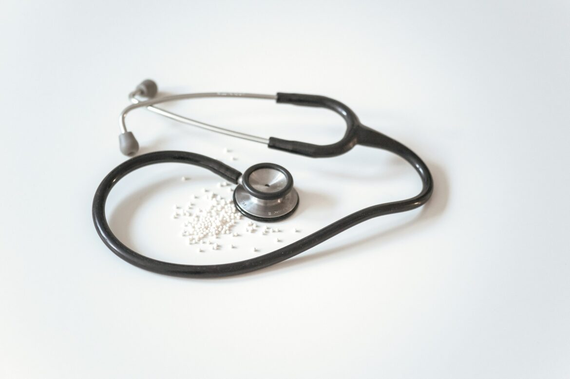 Stethoscope lying on a white surface with scattered white pills nearby.
