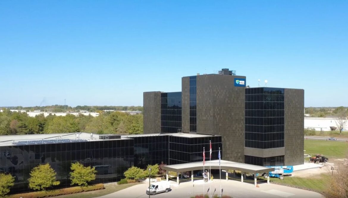 Large dark-glass office building with a curved entrance canopy and flagpoles in front under a clear blue sky.