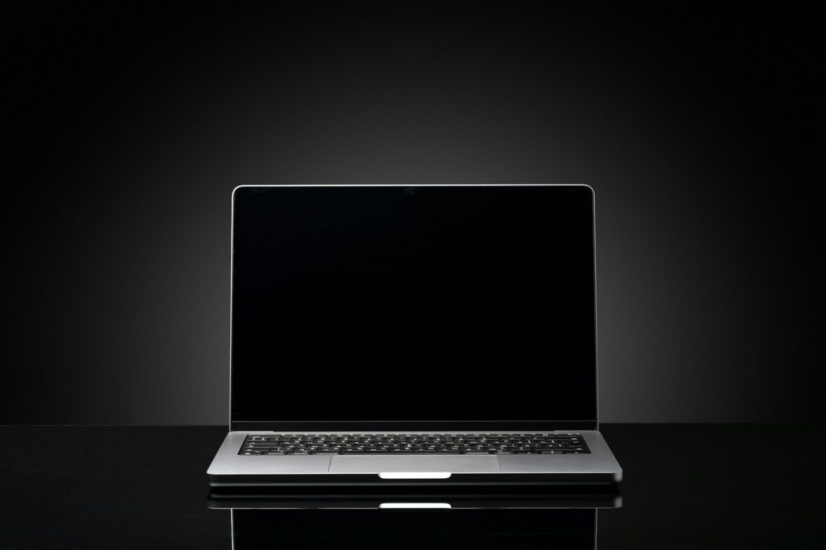 Open silver laptop on a glossy black surface with a dark gradient background, screen off.