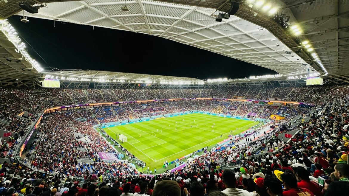Nighttime soccer match in a packed stadium with bright floodlights and fans in the stands.