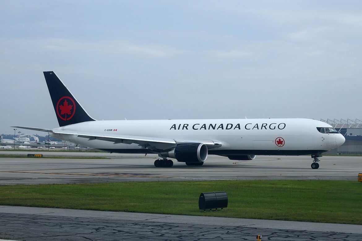 Air Canada Cargo jet on the tarmac, white fuselage, dark tail with red maple leaf logo, engines under the wings, taxiing at the airport.