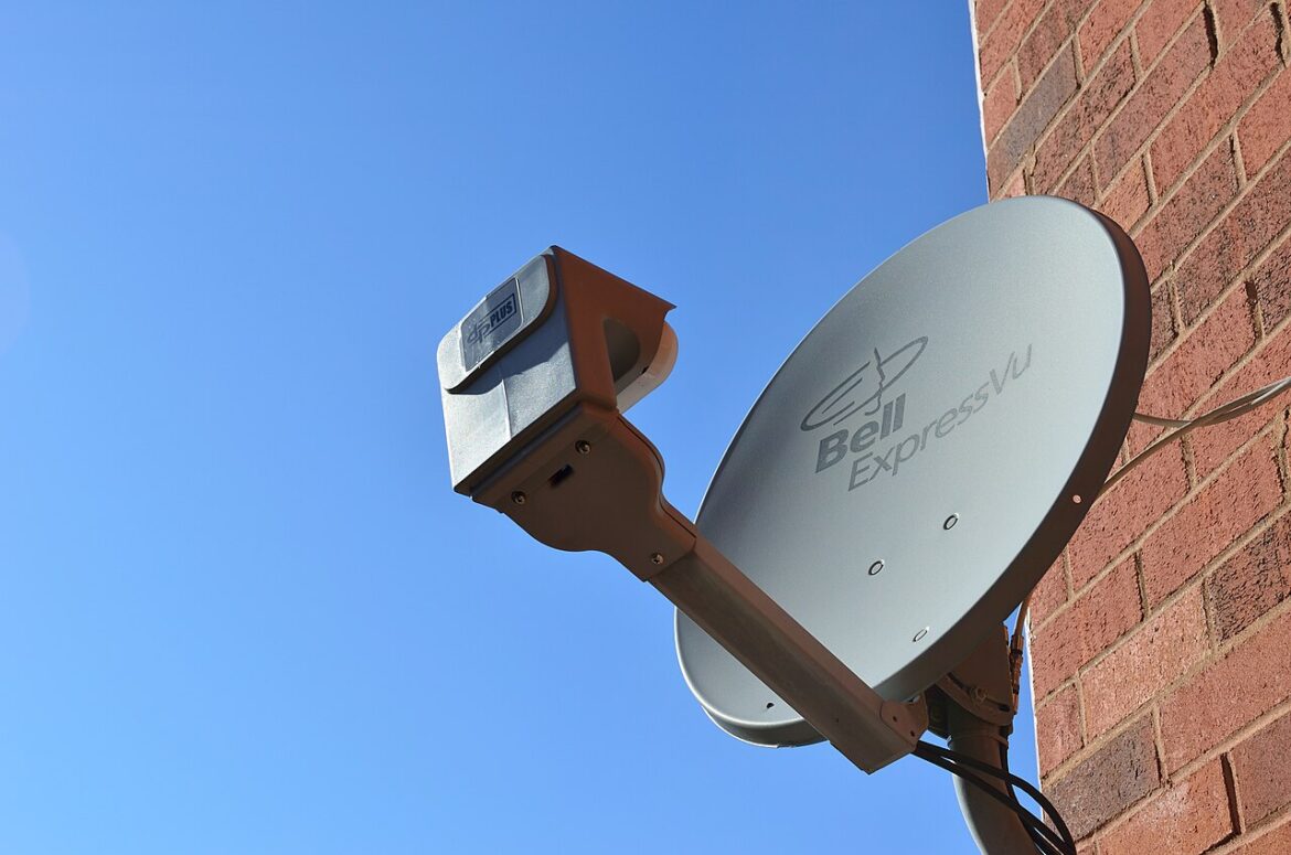 Satellite dish labeled Bell ExpressVu mounted on a brick wall against a clear blue sky.