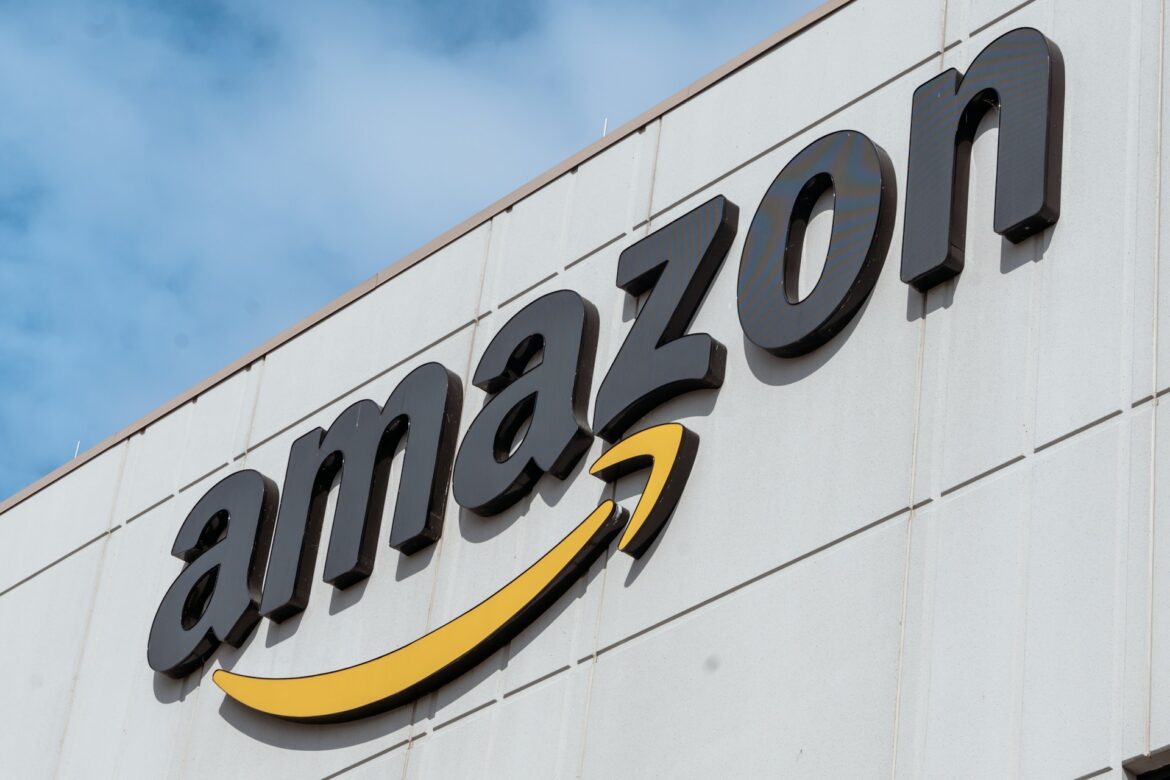 Close-up of the Amazon logo with a yellow curved arrow on a light-gray building wall under a blue sky.