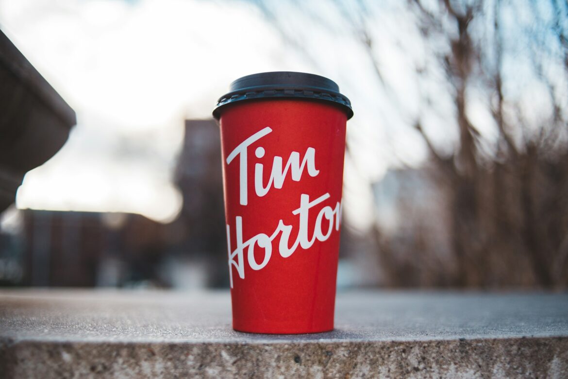 Red Tim Hortons coffee cup with a black lid standing on a stone ledge, outdoors.