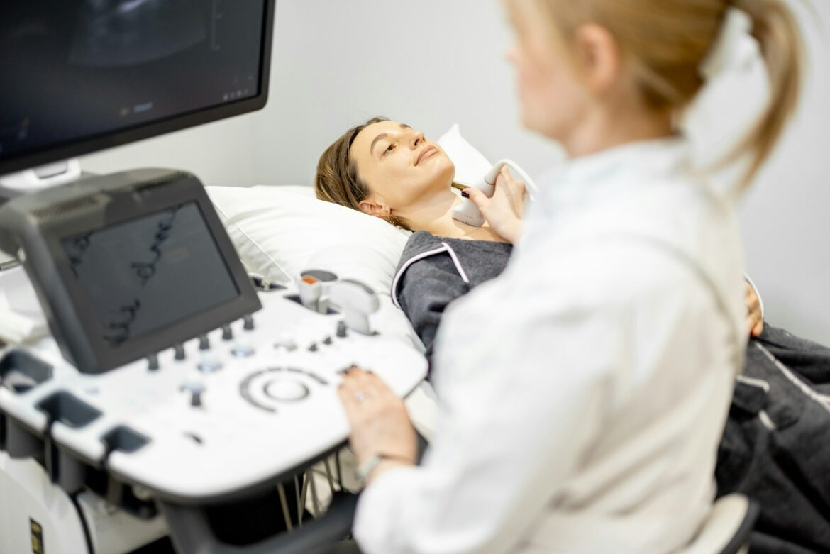 Healthcare professional performing an ultrasound on a patient lying on an exam bed, using a handheld probe on the body area shown.