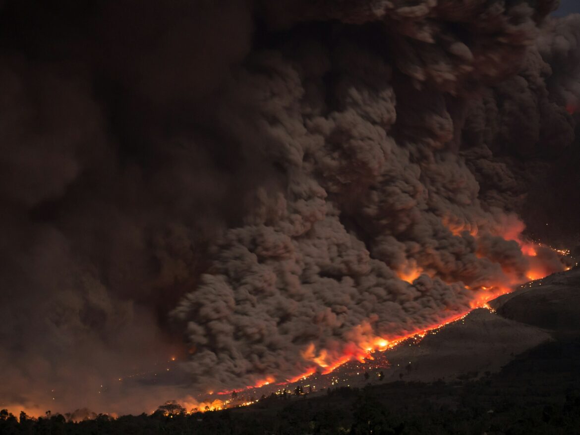 Nighttime volcanic eruption with lava flowing down a hillside and a column of dark ash.