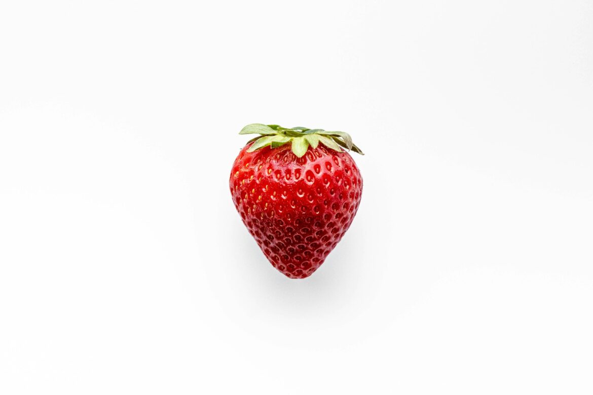 Ripe red strawberry with green leaves on a white background, centered in the image.