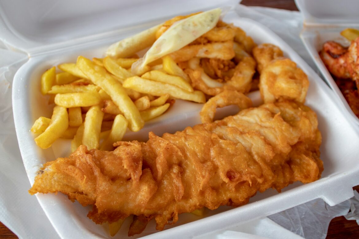 Battered fried fish fillet with French fries in a white takeout tray.