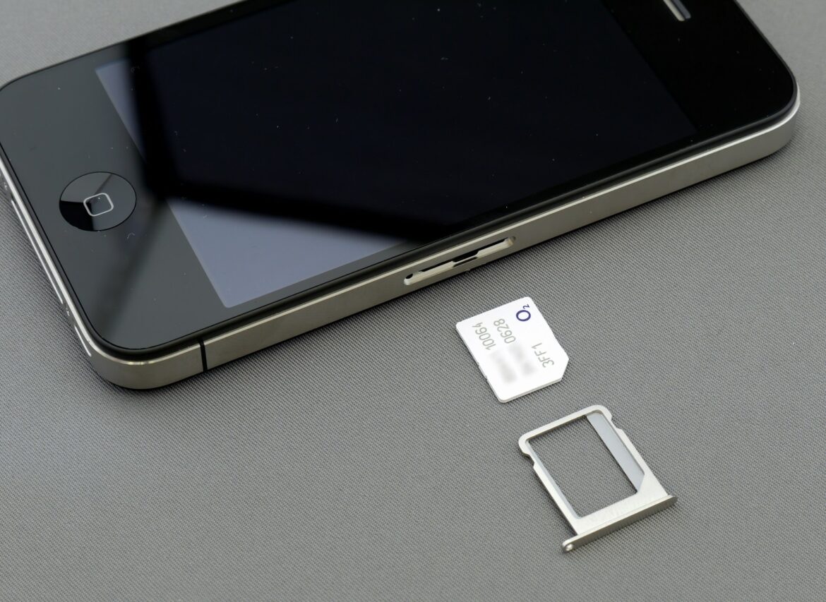 Close-up of a smartphone with a SIM card tray ejected and a SIM card lying nearby on a gray surface.