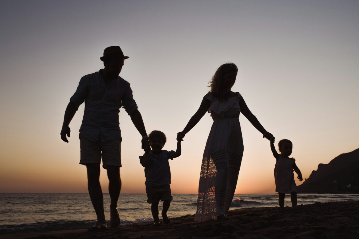 Silhouetted family of five holding hands and walking on a beach at sunset.