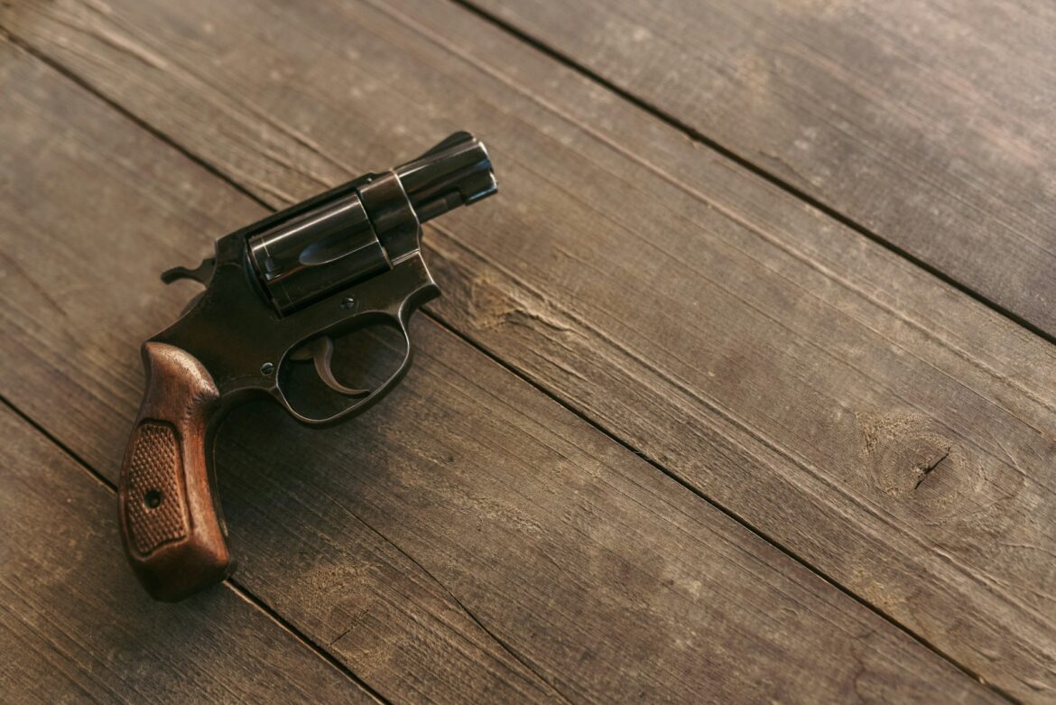 A black revolver with a wooden grip resting on a weathered wooden table surface.