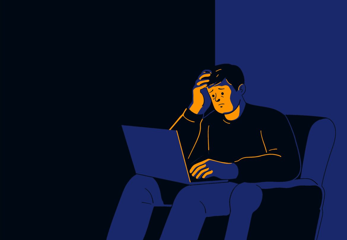 Person sitting on a dark couch with a laptop, head in hand, looking stressed or worried while working remotely.